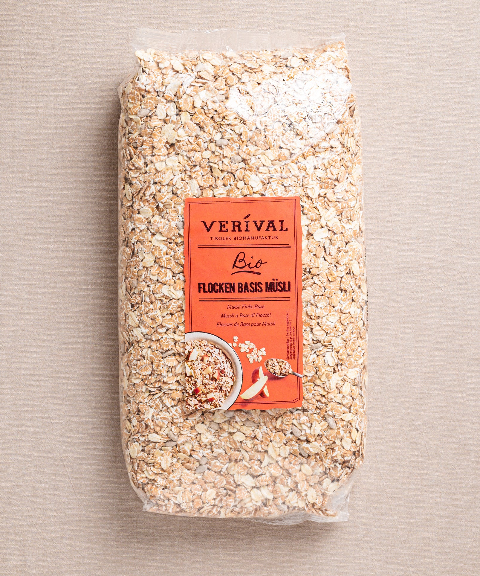 Ein großer Beutel Flocken Basis Müsli von Verival Bio mit rotem Etikett, auf dem nahrhafte Haferflocken und Körner präsentiert werden, ideal für ein vollwertiges Frühstück, präsentiert auf einem neutralen Hintergrund.